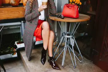 Women wearing red leather skirt and ankle boots with checked long coat. A coffee in her hand. Red hand bag