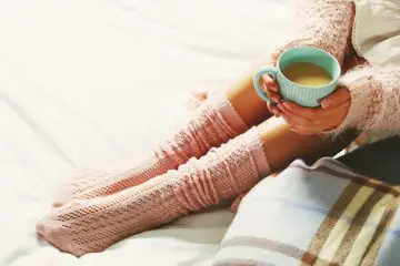 Women wearing pale pink warm knitted leg warmers and coffee cup. Warm sweater on