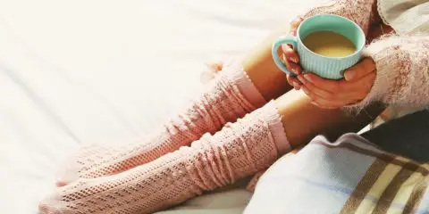Women wearing pale pink warm knitted leg warmers and coffee cup. Warm sweater on