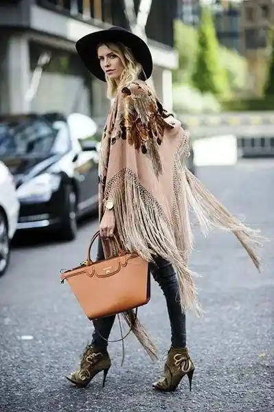 Women wearing a beige poncho with black hat and black skinny jeans with tan handbag