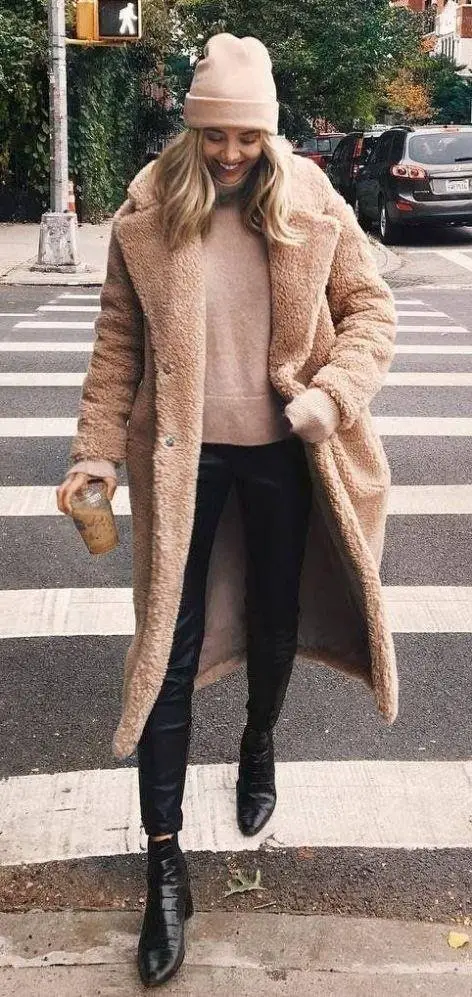 Women wearing winter long beige coat with skinny jeans, oversized jumper and knitted hat