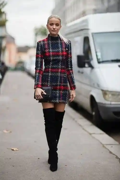 Women wearing short plaid dress with long sleeves and thigh high boots with black clutch bag