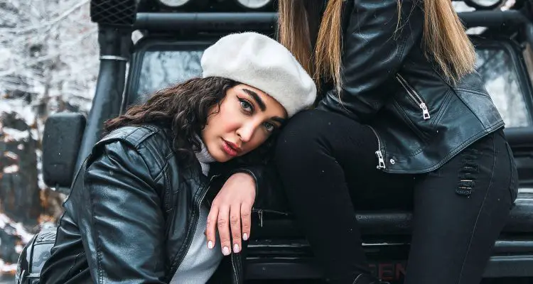 two women in leather jackets and ripped jeans sitting on a car