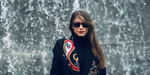 woman wearing a black coat with black sunglasses, red lipstick and scarf